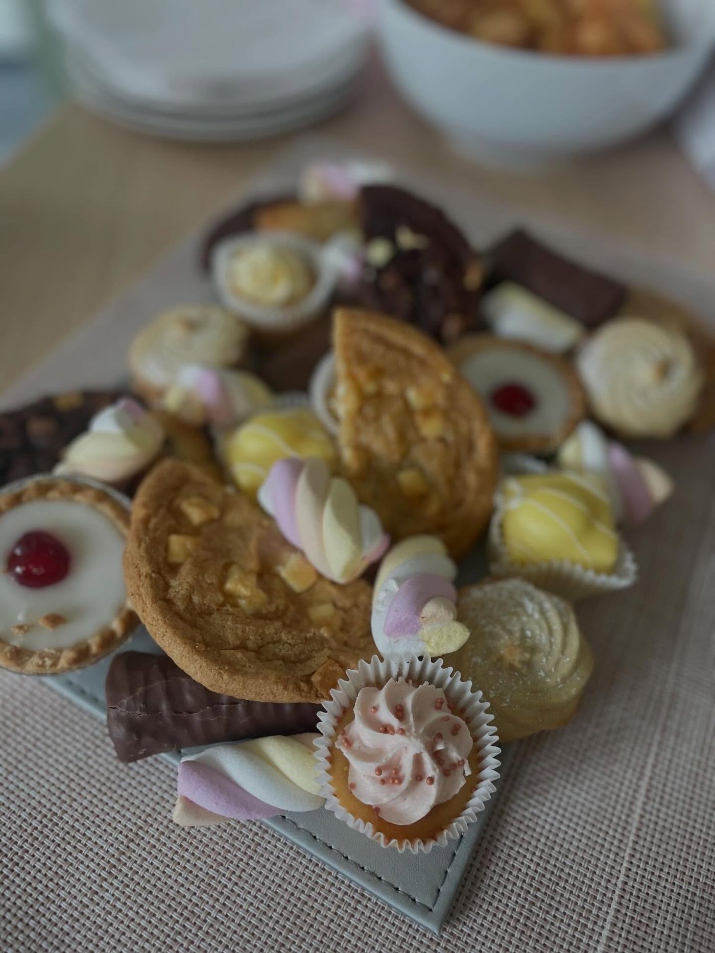 A small sweet board with cookies, Bakewell tarts, a pink cupcake and marshmallow twists