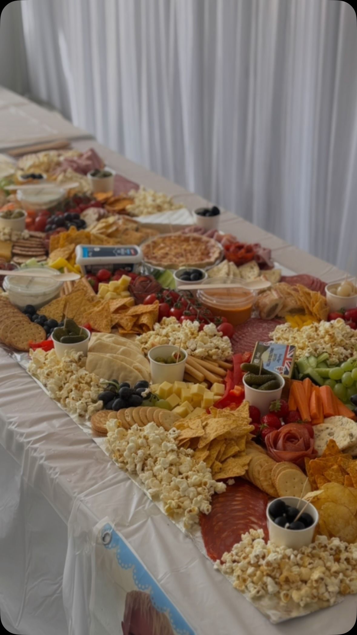 A long grazing table at a christening, with popcorn, crackers, cheese, salami roses and bowls of olives