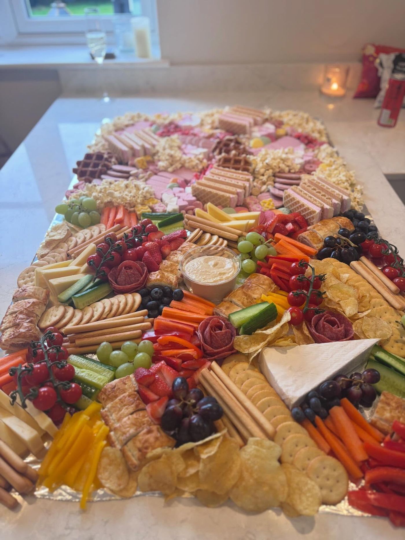 A kitchen island grazing table with pink wafers and sweets at the far end and savoury food at the near end