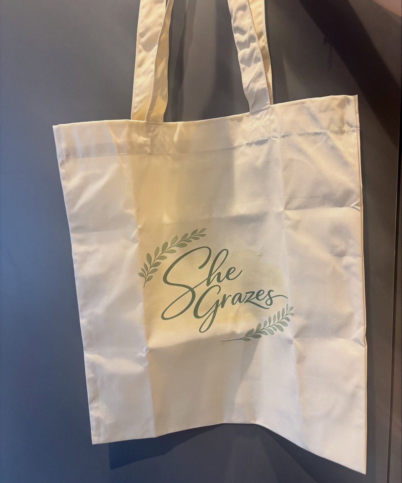 A cream She Grazes tote bag with the sage green logo